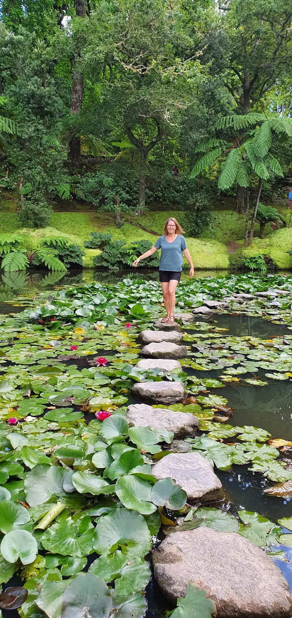 Vrouw op stapstenen tussen waterlelies in een weelderige tuinvijver