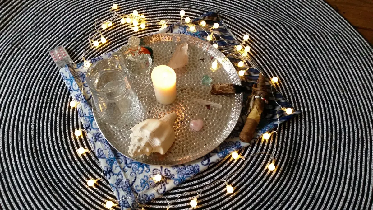 Helend ritueel met een brandende kaars, schelpen en lichtjes op een dienblad