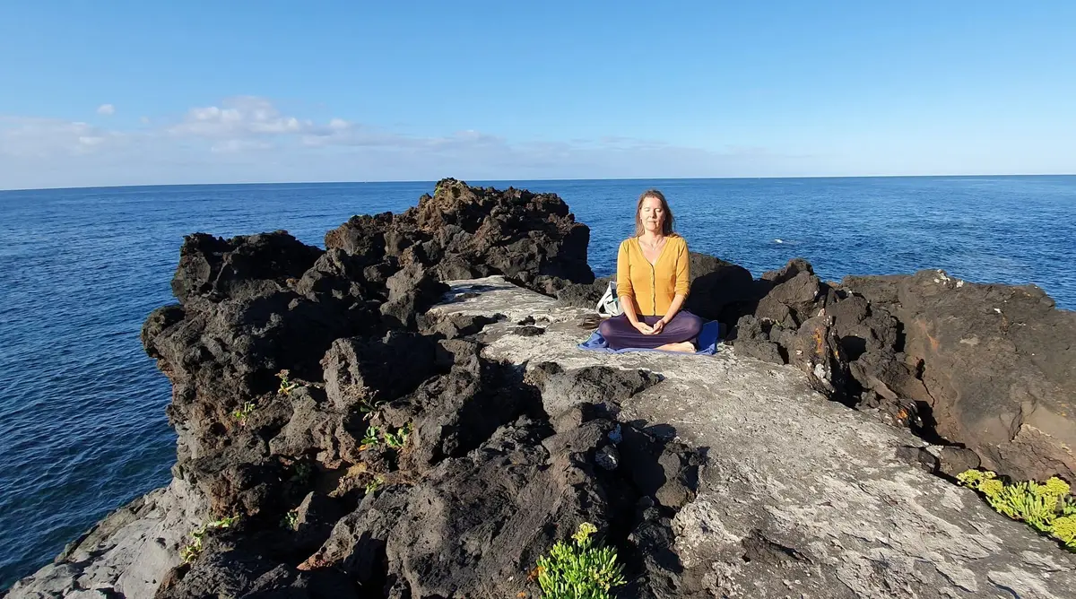 Vrouw in meditatiehouding op de rotsen aan zee